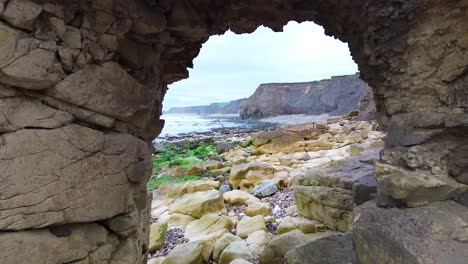 Toma-Aérea-De-Un-Dron-Volando-A-Través-Del-Arco-De-Un-Acantilado-Rocoso-En-La-Playa-De-Ryhope---Sunderland,-Reino-Unido