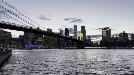 Die-Brooklyn-Bridge-Mit-Den-Lichtern-Von-Manhattan-In-Den-Gebäuden-Am-Wasser-In-Der-Dämmerung