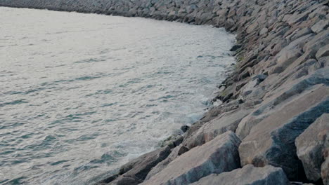 Rocky-shoreline-with-gentle-waves-lapping-against-the-stones-under-a-cloudy-sky