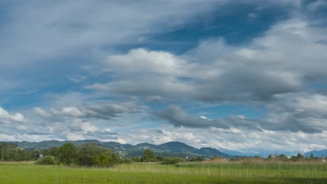 Clouds-move-in-the-blue-sky-over-the-lush-green-natural-landscape-field-in-Switzerland