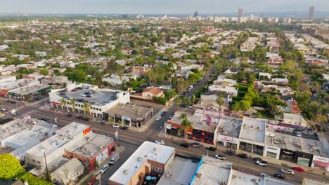 Aerial-Footage-of-Busy-Melrose-Avenue-in-Daytime,-Cars-Driving-Down-Road-with-Colorful-Shops-and-Pedestrians