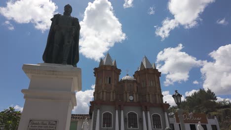 Statue-Und-Historische-Kirche-Unter-Einem-Strahlend-Blauen-Himmel-Mit-Wolken-In-Replica-Del-Viejo-Peñol,-Kolumbien