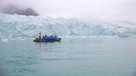 Boat-With-Tourists-Sailing-Under-Glacier-in-Cold-Arctic-Sea-Water,-Slow-Motion