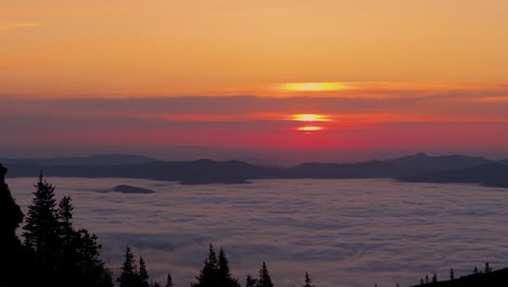 Aerial-close-up-shot-near-mountain-line,-revealing-inversion-clouds-and-the-warm-light-of-the-sunrise-in-the-background