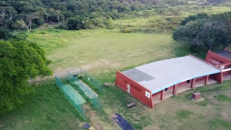 Drones-Volando-Sobre-Redes-De-Entrenamiento-De-Cricket-Y-Un-Antiguo-Edificio-Abandonado,-Vestuarios-Con-Un-Marcador-Blanco-Sobre-Un-Campo-De-Rugby,-Arlequines-En-El-Acantilado-De-Durban