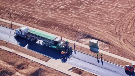 Close-aerial-of-truck-and-asphalt-paving-machine-working-on-a-new-road-at-Silverwoods-Estate