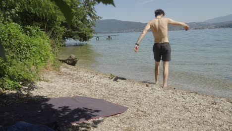 Cucasian-man-enters-cold-water-lake,-Alpine-Europe-static-panoramic-at-daylight