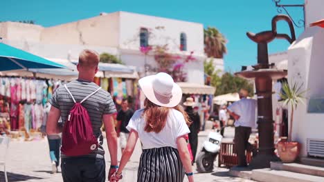 A-man-and-woman-are-walking-arm-in-arm-on-a-street,-wearing-backpacks