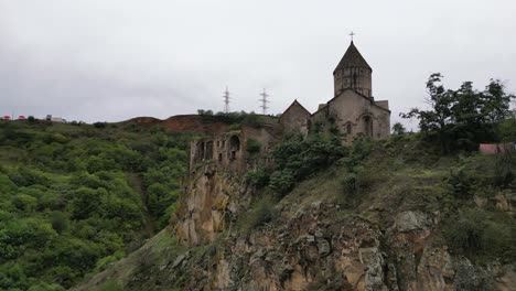 Aerial-ascends-rugged-rock-cliff-to-medieval-Tatev-Monastery,-Armenia