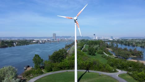 Drone-panning-from-the-left-to-the-right,-showing-a-windmill-in-the-middle-of-the-park-located-in-Danube-Island,-in-Vienna,-Austria