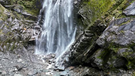 Una-Colosal-Cascada-Que-Cae-Sobre-Montañas-Rocosas-Cubiertas-De-Musgo,-Creando-Un-Fascinante-Espectáculo-Natural