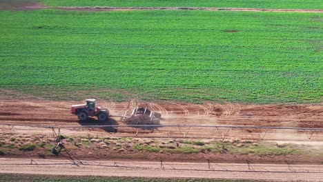 Traktor-Fährt-Auf-Feldweg-Auf-Bauernhof-Neben-Ernte--Und-Bewässerungsgeräten