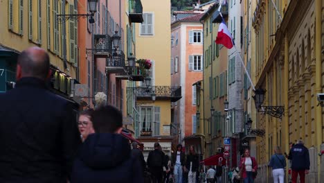 People-walk-in-vibrant-and-narrow-streets-of-Old-Town-Nice,-France-with-colorful-buildings