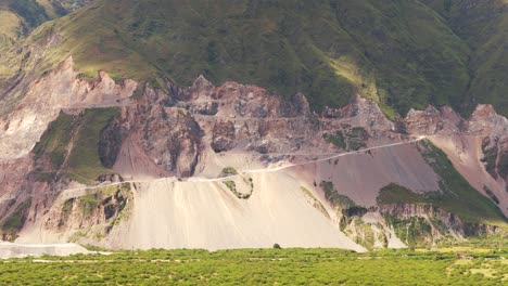 Panoramic-view-zoom-in-to-a-mountain-with-an-arid-road-and-sediments-in-zigzag,-for-transport-and-extraction-of-limestone-in-a-mine-in-the-north-of-Argentina,-Jujuy,-sunny-day