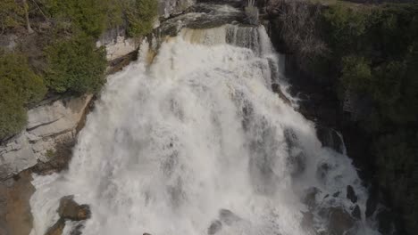 Cascading-waterfall-surrounded-by-rocky-cliffs-and-lush-greenery-in-owen-sound,-aerial-view