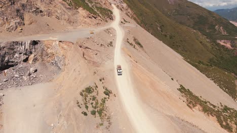 Vista-Aérea-De-Un-Camión-De-Transporte,-Viajando-A-Lo-Largo-De-Un-Camino-De-Tierra-En-El-Borde-De-Una-Montaña-En-Un-Sitio-Minero-De-Piedra-Caliza-En-El-Norte-De-Argentina,-Jujuy