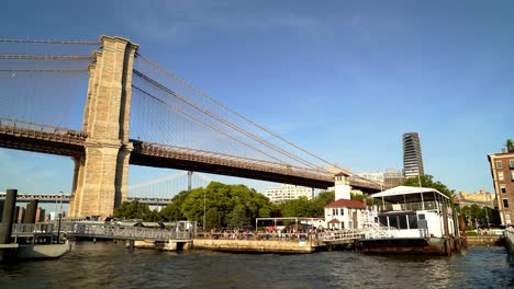 Gente-Haciendo-Fila-Para-Abordar-El-Ferry-Bajo-El-Puente-De-Brooklyn-En-Un-Día-Soleado