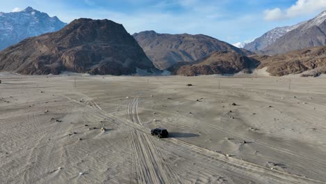 Toma-Aérea-Panorámica-De-Vehículos-De-Turistas-Conduciendo-En-El-Frío-Desierto-De-Sarfaranga---Valle-De-Skardu,-Pakistán