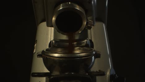 A-close-up-image-of-a-coffee-grinder-dispensing-freshly-ground-coffee-into-a-portafilter,-set-against-a-dark-background