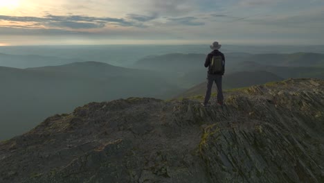 Lone-mountain-walker-on-craggy-mountain-summit-at-golden-hour-facing-setting-sun