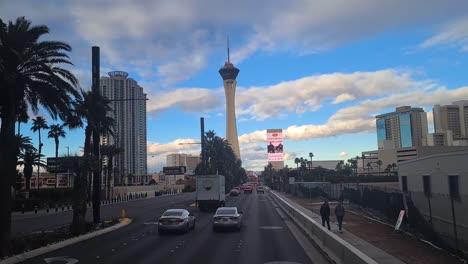 Driving-on-Las-Vegas-Strip-at-Evening,-The-Strat-Hotel-Casino-Tower-in-Background