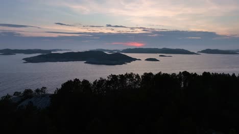 Drone-moves-sideways-over-pine-trees-towards-dramatic-North-Sea-sunset,-creating-parallax-effect-with-coastal-line