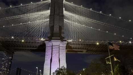 Una-Vista-Hacia-Arriba-Del-Puente-De-Brooklyn-Por-La-Noche,-Que-Muestra-Los-Cables-Iluminados-Y-La-Torre-Del-Puente-Contra-Un-Cielo-Oscuro,-Resaltando-La-Belleza-Arquitectónica-Y-La-Maravilla-De-La-Ingeniería.