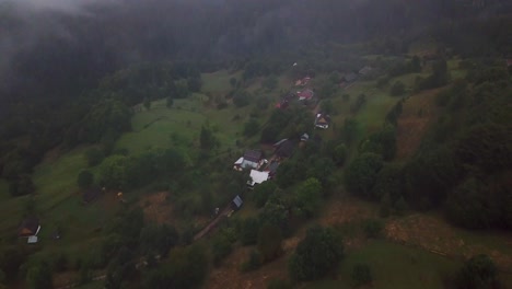 Drone-camera-filming-top-down-the-mountain-village-on-a-foggy-day-in-Matisesti,-Romania