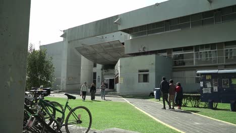 Young-Hispanic-university-students-walking-in-front-of-the-facade-of-the-Metropolitan-Autonomous-University-of-Xochimilco,-Mexico