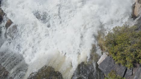 Powerful-waterfall-rushing-over-rocky-cliffs-surrounded-by-lush-greenery-in-owen-sound,-aerial-view