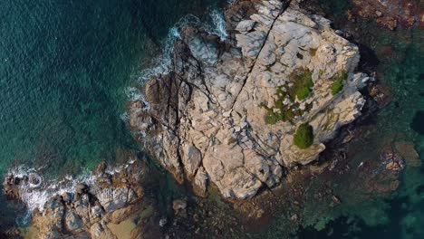 Stunning-overhead-drone-footage-of-a-rocky-island-in-the-Mediterranean-Sea-with-vibrant-blue-and-turquoise-waters,-captured-from-below-and-ascending