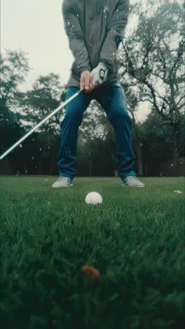 Male-golfer-stands-on-fairway-in-downpour,-swings-and-chips-golf-ball-in-slow-motion-and-water-splashes-everywhere