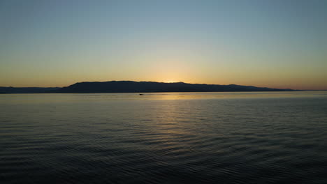 Barco-En-Silueta-Navegando-A-Lo-Lejos-A-Través-Del-Lago-Flathead-En-Montana-Al-Atardecer-En-Verano