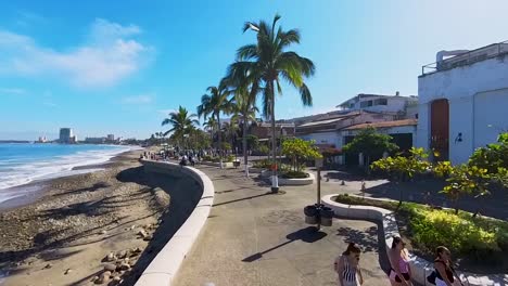 Tourists-walking-along-the-beach-and-boardwalk-in-Puerto-Vallarta,-Mexico-on-a-sunny-day