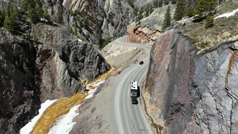 Top-Down-View-of-an-RV-Towing-a-Jeep,-Driving-through-a-winding-gorge,-next-to-a-gold-colored-river,-Million-Dollar-Highway,-Uncompahgre-river,-Ouray-Colorado