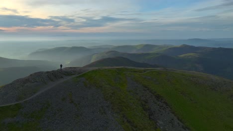 Distant-lone-mountain-walker-silhouetted-against-golden-hour-lit-misting-valley