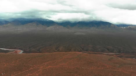 Aerial-shot-of-a-barren-landscape-in-Utah,-on-an-overcast-day-with-snow-covered-mountains-in-the-background