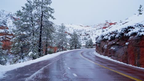 Red-roads-in-Zion-National-park-in-the-winter-after-a-fresh-snowfall-with-evergreen-Pine-trees-and-Mountain-tops-in-the-background