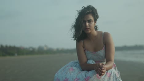 An-attractive-young-indian-lady-woman-is-sitting-on-the-tropical-beach-in-a-dress