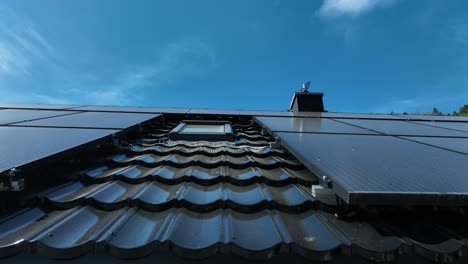 Low-angle-view-looking-up-a-solar-panel-array-installed-on-metal-roof-of-house,-tracking-right-to-left