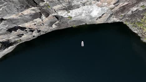 Drone-descends-towards-a-rib-boat-near-a-dramatic-towering-mountain-wall-in-a-Norway-fjord