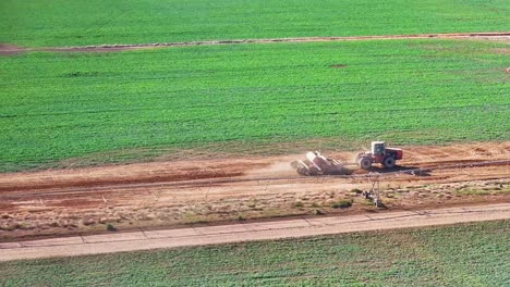 Tractor-and-small-road-grader-working-along-a-dirt-road-beside-irrigation-equipment