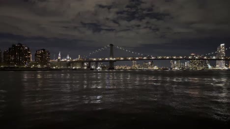 Ein-Ruhiger-Nächtlicher-Blick-Auf-Den-East-River-Mit-Der-Beleuchteten-Manhattan-Bridge-Vor-Der-Kulisse-Der-Skyline-Der-Stadt,-Der-Die-Ruhige-Schönheit-Der-Städtischen-Nacht-Einfängt