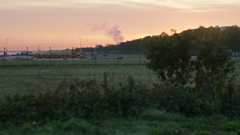 Flughafen-München-Im-Morgenlicht-Mit-Einem-Orangefarbenen-Himmel-Und-Nebel-Auf-Der-Landebahn-Durch-Den-Zaun-Von-Außen-Gesehen