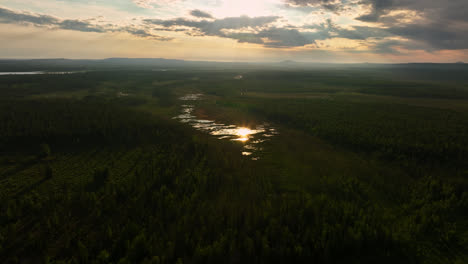 Aerial-view-away-from-a-reflecting-swamp,-sunny,-summer-evening,-in-Lapland