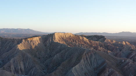 Aerial-view-of-the-rugged-and-dramatic-Anza-Borrego-Badlands,-showcasing-the-unique-geological-formations-and-textures-of-the-eroded-landscape-under-a-clear-sky-during-golden-hour