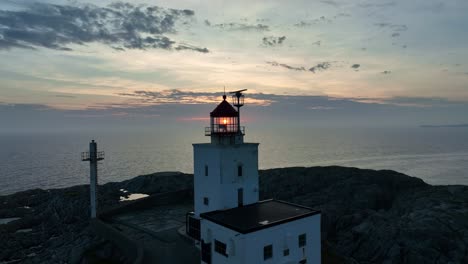 Marsteinen-Lighthouse-on-the-Norwegian-coast,-with-sun-illuminating-through-the-lighthouse-glass,-aerial