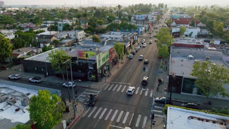 Flying-Over-Melrose-Avenue,-Drone-Footage-of-Cars-Driving-Along-Busy-Iconic-West-Hollywood-Street-in-Shopping-District