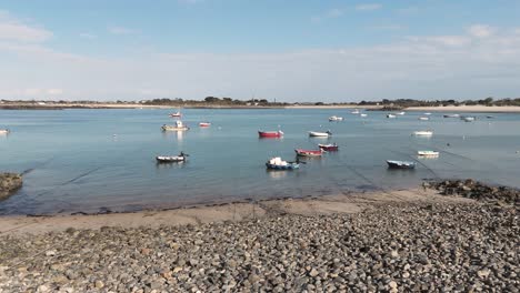 Slow-low-drone-flight-from-shoreline-towards-bay-in-Guernsey-with-boats-at-anchor-crystal-clear-water-and-golden-beaches-on-bright-sunny-calm-day