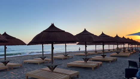 Beautiful-evening-sunset-beach-with-sun-beds,-tiki-umbrellas,-sea-view,-sand-and-kids-playing,-people-walking,-holiday-vacation-in-Marbella-Spain,-4K-shot